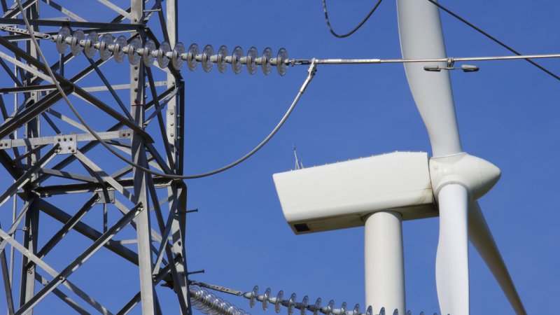 A high-power electrical transmission tower on the background of a wind turbine. (Source: © pedrosala / stock.adobe.com)